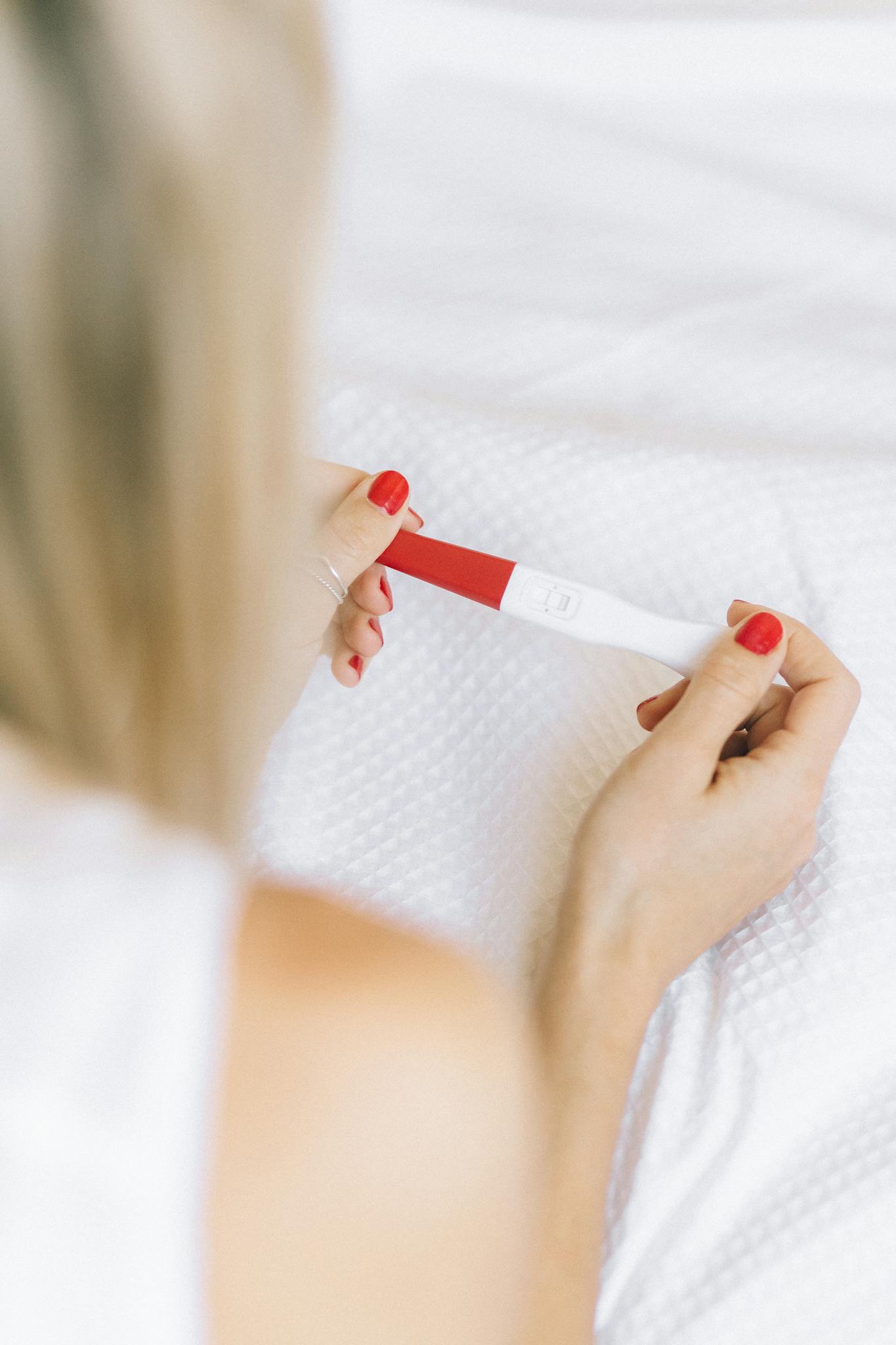 Close-up of a woman holding a positive pregnancy test, showcasing manicured nails.