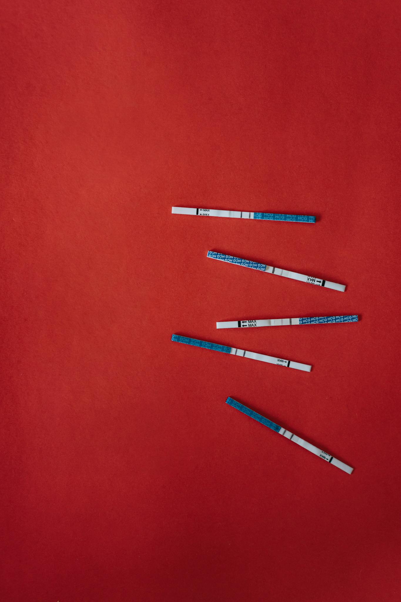 Pregnancy test strips arranged on a vivid red background, symbolizing health and biology.